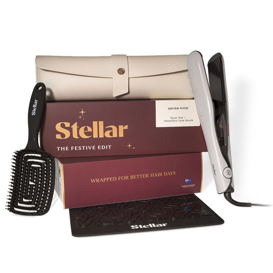 Stellar The Festive Edit hair care gift set featuring a silver flat iron, black paddle brush, black comb guard, and cream-colored storage case, arranged in front of branded burgundy and gold packaging boxes on a white background.